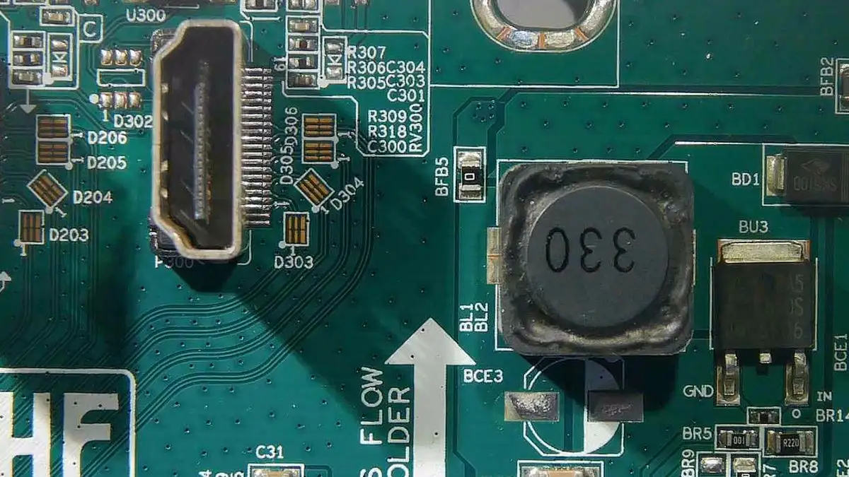 Vue au microscope de composants montés en surface sur une carte de moniteur, pastilles et soudures visibles au détail.
